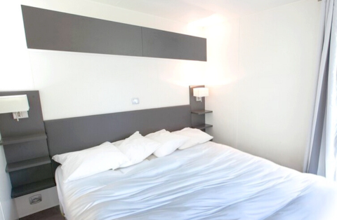 Modernes Schlafzimmer mit Doppelbett und weißen Wänden in der Stacaravan Premium, Flower Camping L'Ile d'Offard.