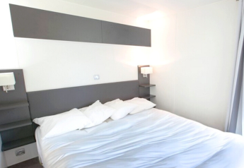 Chambre moderne avec lit double et murs blancs à Stacaravan Premium au Flower Camping L'Ile d'Offard, France.
