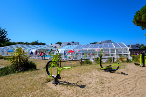 Appareils de fitness extérieurs et piscine couverte au Flower Camping Le Bois d'Amour en Bretagne, France.