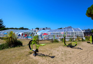 Outdoor fitness equipment and covered swimming pool at Flower Camping Le Bois d'Amour in Brittany, France.
