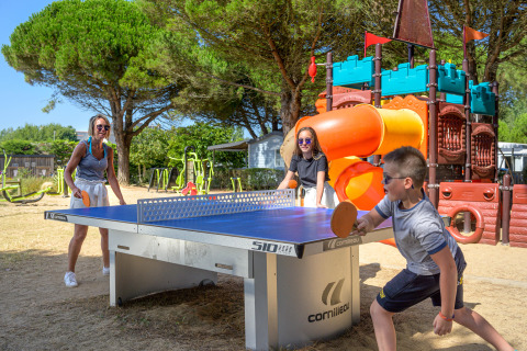Familia jugando al ping-pong al aire libre junto a un parque infantil en Flower Camping Le Bois d'Amour, Bretaña.