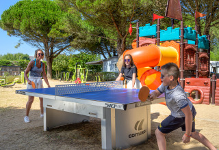 Family playing table tennis outdoors near a playground at Flower Camping Le Bois d'Amour, Brittany.