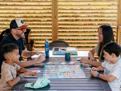 Familia jugando a un juego de mesa en Flower Camping Le Bois d'Amour, un parque vacacional en Bretaña, Francia.