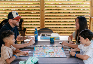 Familia jugando a un juego de mesa en Flower Camping Le Bois d'Amour, un parque vacacional en Bretaña, Francia.