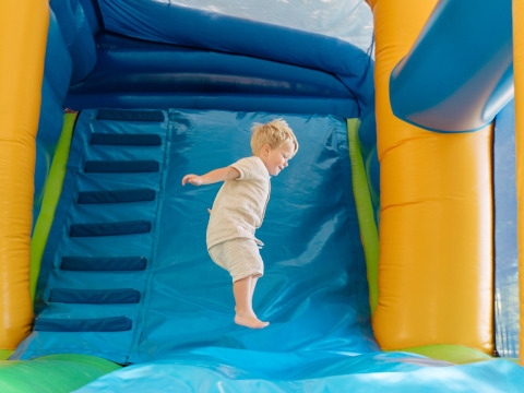 A young child jumps on a blue inflatable bouncy castle at Flower Camping Le Bois d'Amour in Brittany, France.