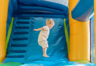 A young child jumps on a blue inflatable bouncy castle at Flower Camping Le Bois d'Amour in Brittany, France.