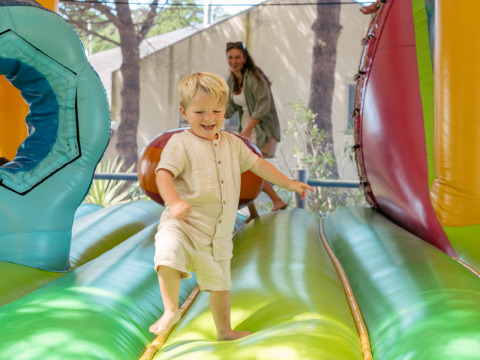 Un niño sonriente juega en un hinchable colorido con un adulto detrás en Flower Camping Le Bois d'Amour, Bretaña.