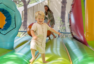 Un niño sonriente juega en un hinchable colorido con un adulto detrás en Flower Camping Le Bois d'Amour, Bretaña.