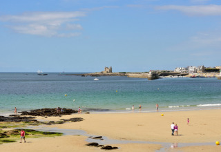 Personas disfrutan de un día soleado en la playa cerca de Quiberon, Bretaña, con castillo y mar al fondo.