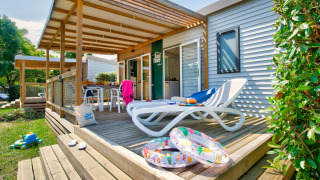 Zonnig terras bij chalet met ligzetel, opblaasbanden, kinderspeelgoed en gezellige zithoek buiten.