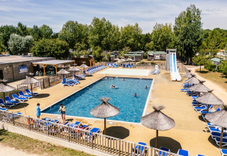 Udendørs swimmingpoolområde med liggestole og parasoller på Camping Demoiselles Plage i Pays de la Loire, Frankrig.