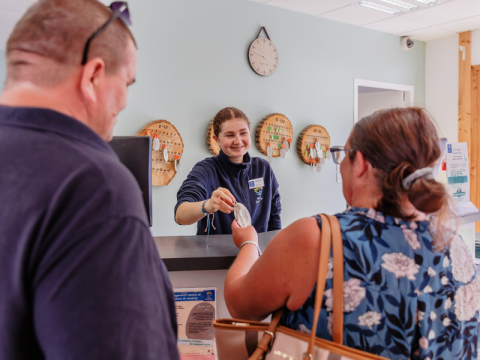 Receptionist hands key to guests at Camping Demoiselles Plage holiday park in Pays de la Loire, France.
