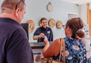 Receptionist udleverer værelsesnøgle til gæster på Camping Demoiselles Plage i Pays de la Loire, Frankrig.