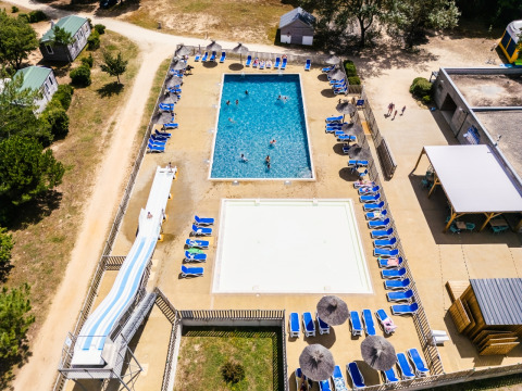 Vista aerea della zona piscina con lettini, scivolo e bungalow al Camping Demoiselles Plage, Francia.