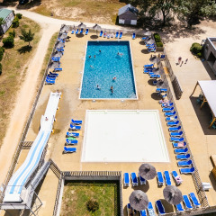 Luchtfoto van het zwembad met ligstoelen, glijbaan en chalets op Camping Demoiselles Plage, Frankrijk.