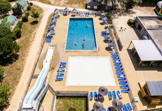 Vista aerea della zona piscina con lettini, scivolo e bungalow al Camping Demoiselles Plage, Francia.