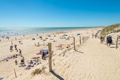 People relaxing on the sandy beach at Camping Demoiselles Plage, Pays de la Loire, France, under a clear sky.