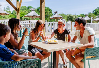 Family enjoying lunch together outdoors in the sun at Camping Demoiselles Plage, Pays de la Loire, France.