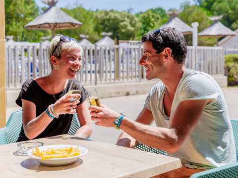Two happy people enjoy drinks and fries outdoors at Camping Demoiselles Plage in Pays de la Loire, France.