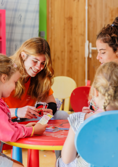 Twee kinderen en twee volwassenen spelen een kaartspel in de binnenspeelruimte van Camping Demoiselles Plage.