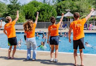 Four activity leaders in orange shirts lead a poolside group at Camping Demoiselles Plage, France.