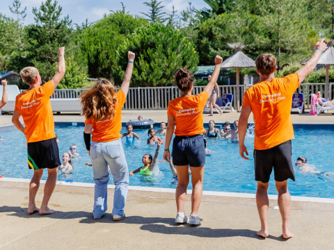 Four activity leaders in orange shirts lead a poolside group at Camping Demoiselles Plage, France.