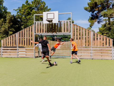 Bambini giocano a calcio su un campo verde recintato in legno al Camping Demoiselles Plage in Francia.