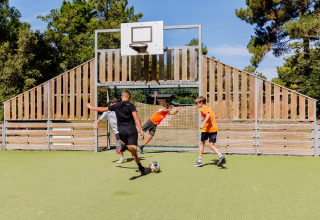 Bambini giocano a calcio su un campo verde recintato in legno al Camping Demoiselles Plage in Francia.