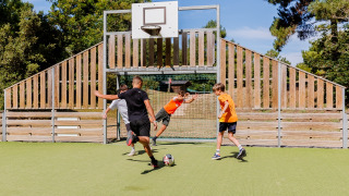 Children play a game of soccer on a green field with a wooden fence at Camping Demoiselles Plage, France.