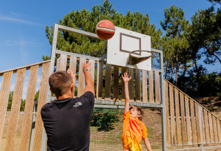 Dos personas juegan baloncesto al aire libre en Camping Demoiselles Plage, Pays de la Loire, Francia, bajo cielo azul.