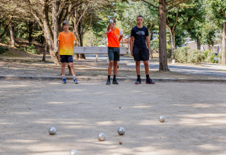 Tre giovani giocano a pétanque su un campo sabbioso circondato da alberi al Camping Demoiselles Plage, Francia.