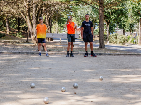 Tre giovani giocano a pétanque su un campo sabbioso circondato da alberi al Camping Demoiselles Plage, Francia.