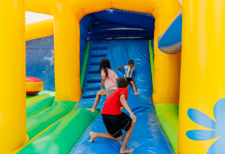 Children playing on a colorful inflatable slide at Camping Demoiselles Plage holiday park in France.