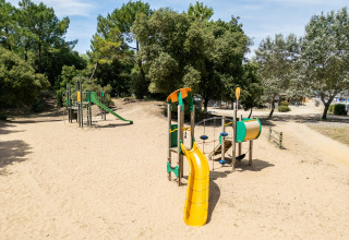 Playground with slides and climbing structures on sand, surrounded by trees at a holiday park in Pays de la Loire.