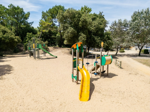 Legeplads med rutsjebane og klatrestativer omgivet af sand og træer i en feriepark i Pays de la Loire.