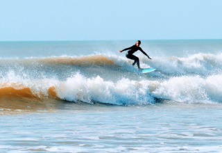 A surfer rides a wave near Saint-Hilaire-de-Riez, Pays de la Loire, France, with clear blue skies overhead.