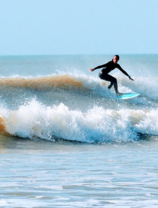 Un surfista cavalca un'onda vicino a Saint-Hilaire-de-Riez, Pays de la Loire, Francia, sotto un cielo limpido.