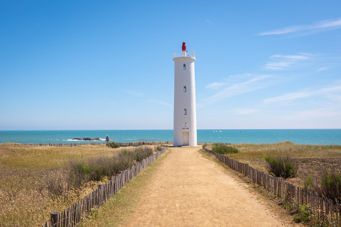 Højt fyrtårn ved havet nær Saint-Hilaire-de-Riez, med blå himmel og grussti, Pays de la Loire.