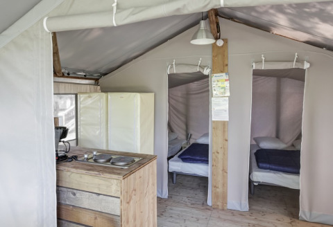 Interior of a safari tent with two single beds, a simple kitchenette, wooden floor and canvas walls.