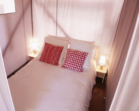 Photo of a cozy bed with red pillows and bedside lamps inside a safari tent with fabric walls.