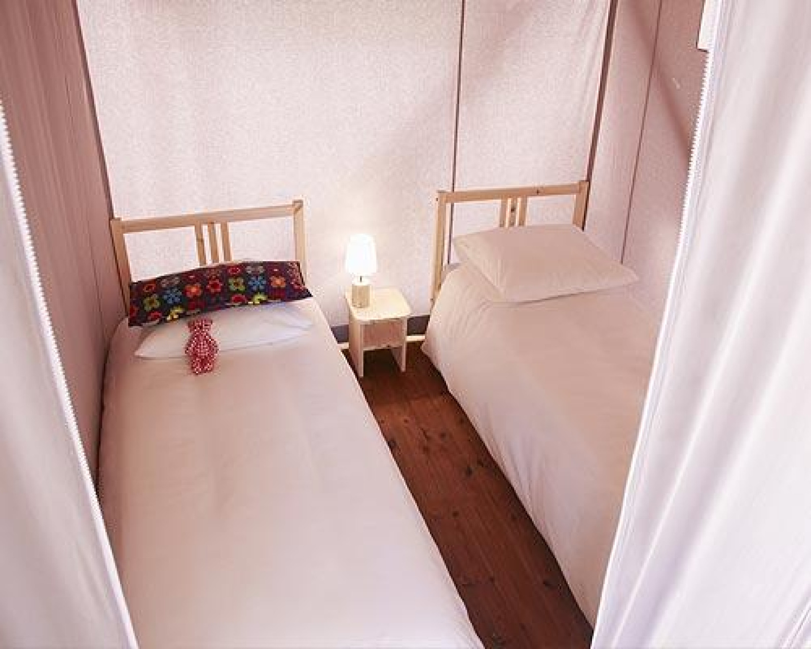 Interieur van een safaritent met twee eenpersoonsbedden, een nachtkastje met lamp en houten vloer.