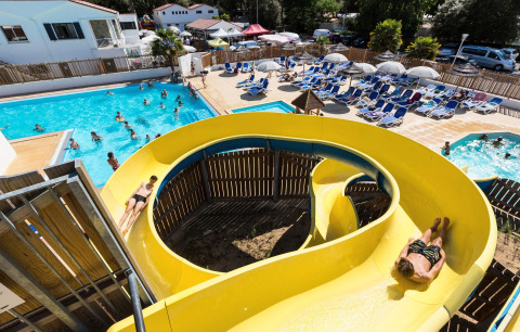 Vacanciers profitent d’un toboggan jaune, piscine et transats à Flower Camping Les Dunes, Pays de la Loire, France.