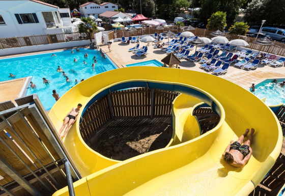 Feriegæster nyder vandland med gul rutsjebane, pool og solsenge på Flower Camping Les Dunes i Frankrig.