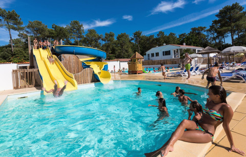 People enjoying waterslides and relaxing by the pool at Flower Camping Les Dunes in Pays de la Loire, France.