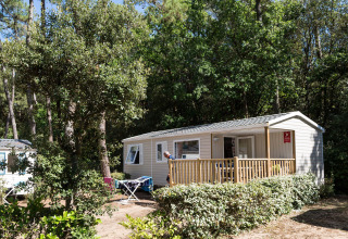 Mobile home nestled among trees at Flower Camping Les Dunes, Pays de la Loire, France, on a sunny day.
