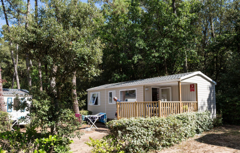 Mobilhome blandt træer på Flower Camping Les Dunes i Pays de la Loire, Frankrig, solrig dagstemning.