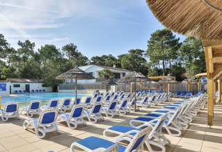 Zona de piscina al aire libre con tumbonas azules y sombrillas de paja en Flower Camping Les Dunes, Pays de la Loire, Francia.