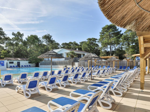 Außenpoolbereich mit blauen Liegestühlen und Strohdächern im Flower Camping Les Dunes in Pays de la Loire, Frankreich.