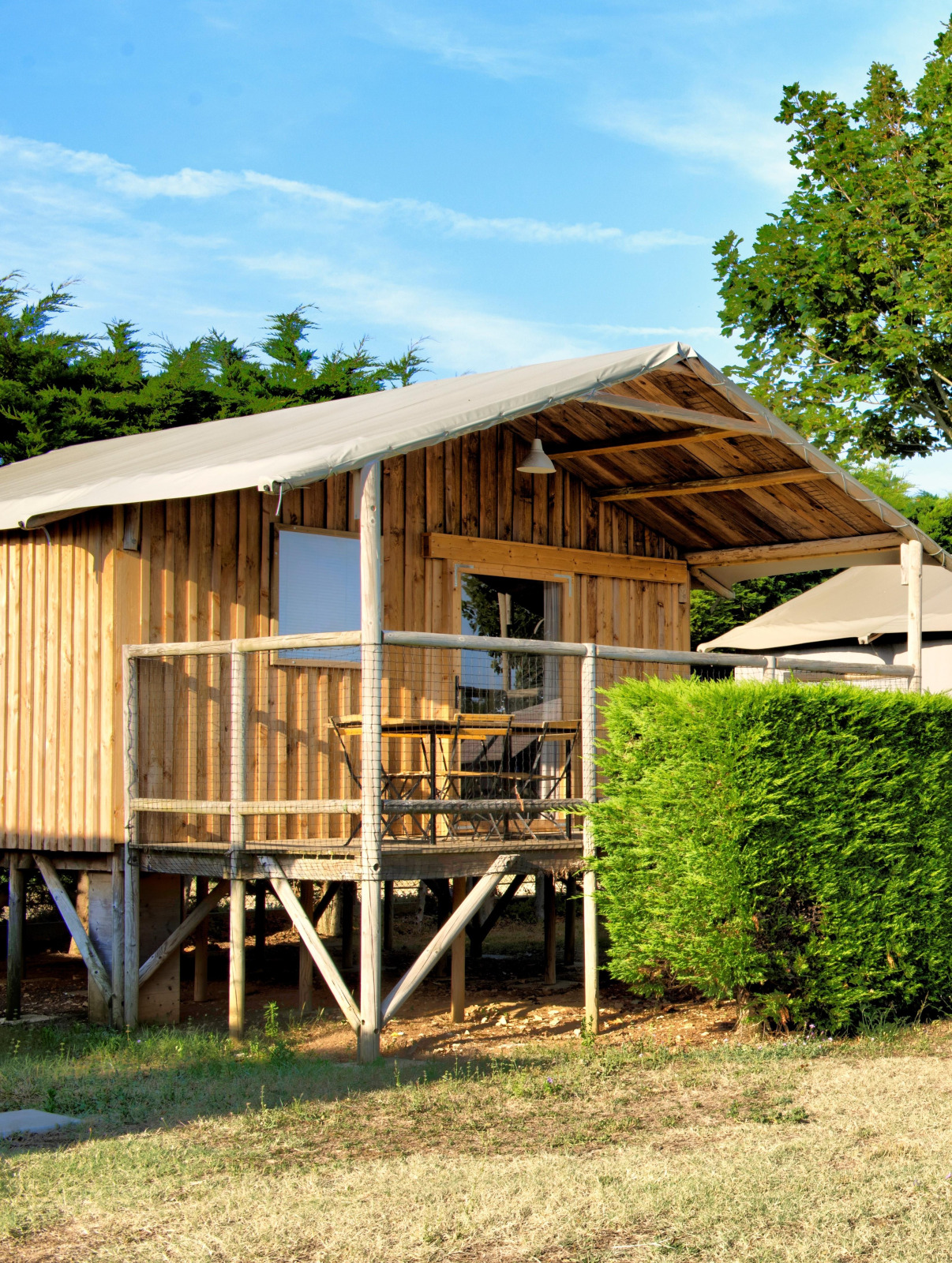Safaritent Cabane Lodge met sanitair bij Flower Camping Les Ilates in Frankrijk, houten veranda zichtbaar.