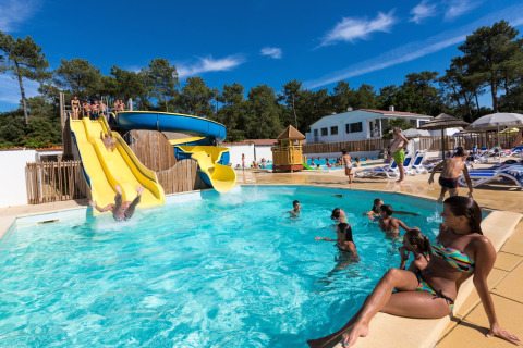 Gezinnen genieten van het zwembad met glijbaan bij Flower Camping Les Dunes in Pays de la Loire, Frankrijk.